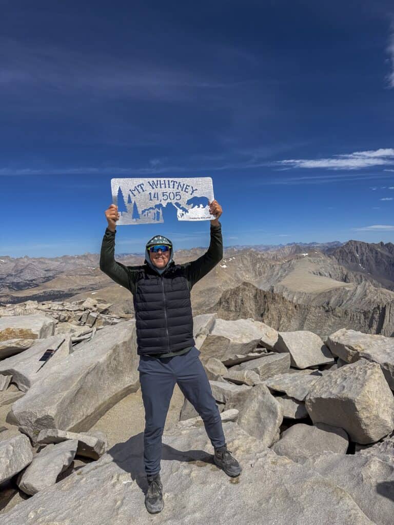 Hiker standing on the summit of Mount Whitney with panoramic Sierra Nevada views on our Cottonwood to Mt. Whitney to Shepherd Pass Guided Hike