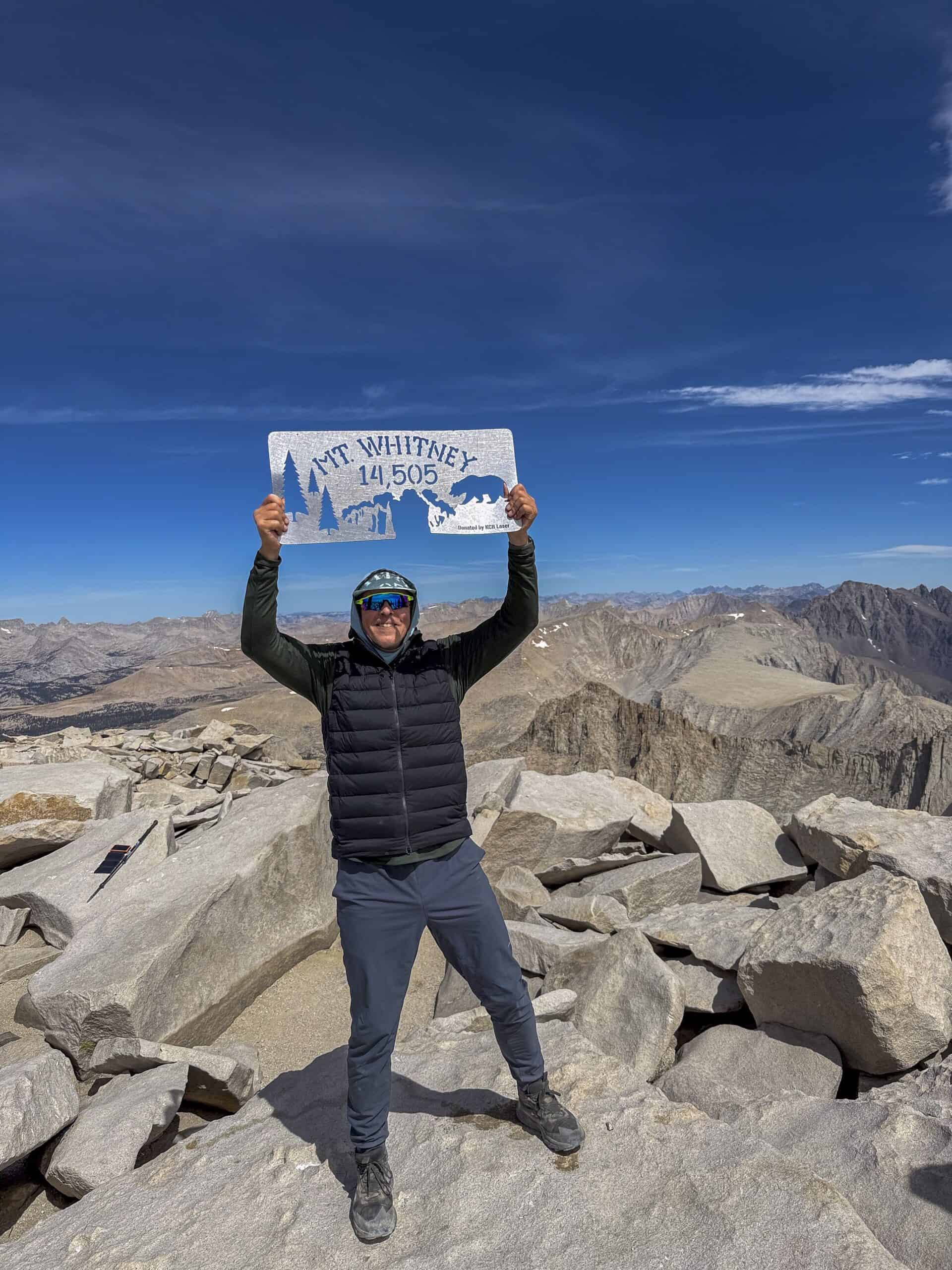 Hiker standing on the summit of Mount Whitney with panoramic Sierra Nevada views on our Cottonwood to Mt. Whitney to Shepherd Pass Guided Hike